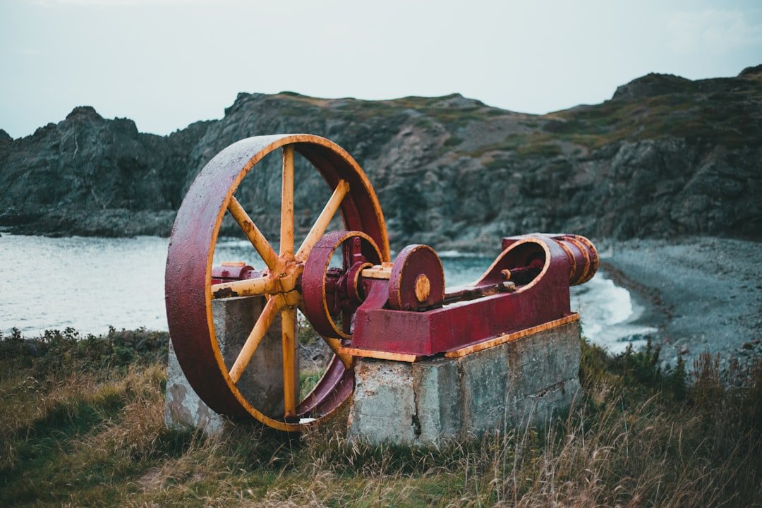 an old rusted water pump sitting in a field next to a body of water